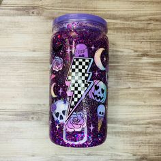 a purple glitter tumbler with skulls, roses and lightning bolt on the side is sitting on a wooden surface