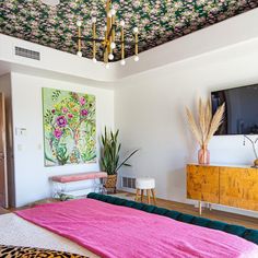 a bedroom with pink and green bedding, leopard print throw pillow, gold chandelier