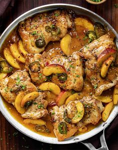 a pan filled with chicken and peaches on top of a wooden table