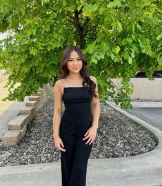 a woman standing in front of a tree wearing a black strapless jumpsuit and heels