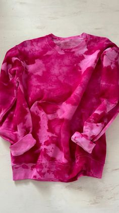 a pink tie - dyed sweatshirt laying on a white surface