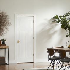 a dining room table and chairs in front of a door with potted plants on it