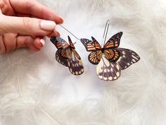 two butterflies are being held by someone's hand on a white fur covered surface