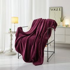 a chair with a blanket on it in front of a white wall and floor lamp