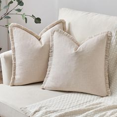 two white pillows sitting on top of a couch next to a plant in a vase