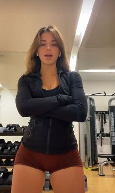 a woman is standing in the gym with her arms crossed and looking at the camera