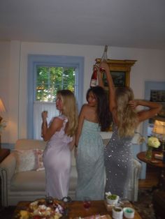 three women standing in a living room next to a table with food and drinks on it