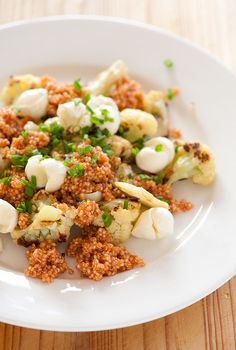 a white plate topped with cauliflower covered in sauce and seasoning next to a wooden table