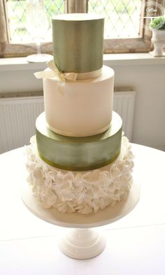 a three tiered wedding cake sitting on top of a white table next to a window