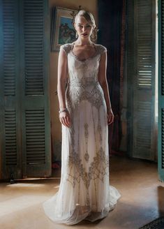 a woman in a long white dress standing next to a doorway and looking at the camera