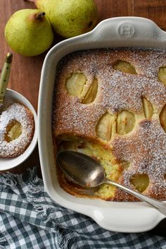 an apple cobbler with powdered sugar on top and two pears next to it