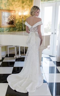 a woman standing in front of a piano wearing a wedding dress with an off the shoulder bow