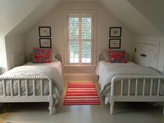 two twin beds in a bedroom with white walls and flooring, along with a red rug on the floor