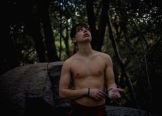 a shirtless man standing in the woods