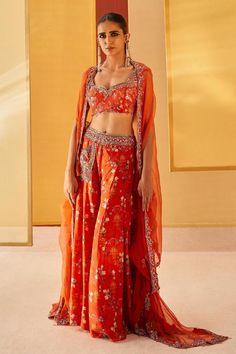 Orangish red silk organza cape with floral print and zardosi and pitta embroidery. Comes with sharara and a blouse.
Components: 3
Pattern: Printed, Embroidered
Type Of Work: Floral, Zardosi, Pitta
Neckline: Sweetheart
Sleeve Type: Cape : Flared Sleeves, Blouse : Sleeveless
Fabric: Silk organza
Color: Orange,Red
Other Details: 
Pocket detailing on sharara
Note : Outfit worn by the model on the left is not for sale.
Occasion: Mehendi and Haldi - Aza Fashions Bollywood Style Embroidered Sets With Traditional Drape, Bollywood Sets With Embroidery And Traditional Drape, Bollywood Embroidered Sets With Traditional Drape, Red Saree Set With Floral Embroidery, Semi-stitched Orange Sets With Motifs, Red Floral Embroidered Saree Set, Red Anarkali Set With Floral Embroidery For Festivals, Red Floral Embroidery Anarkali Set For Festivals, Red Floral Embroidered Sets For Navratri