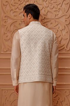 Cream bundi with floral embroidery. Paired with draped kurta and churidar.
Component: 3
Pattern: Embroidered
Type Of Work: Floral
Neckline: Band
Sleeve Type: Bundi: Sleeveless, Kurta: Full Sleeves
Fabric: Bundi: Raw Silk, Kurta and Churidar: Crepe Silk
Color: Cream
Other Details: 
Floral motifs
Front buttons
Embroidered placket
Occasion: Wedding - Aza Fashions Elegant Nehru Jacket With Chikankari Embroidery In Cotton Silk, Elegant Cotton Silk Nehru Jacket With Chikankari Embroidery, Designer Sleeveless Raw Silk Kurta, Sleeveless Kurta With Resham Embroidery For Wedding, Elegant Cotton Silk Nehru Jacket With Resham Embroidery, Sleeveless Wedding Kurta With Cutdana, Wedding Sleeveless Kurta With Cutdana, Fitted Bollywood Nehru Jacket With Resham Embroidery, Sleeveless Kurta With Zari Work For Reception