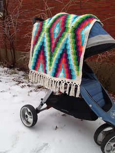 a baby stroller with a colorful blanket on it's back in the snow