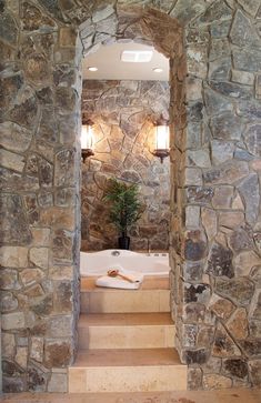 a bathroom with stone walls and steps leading up to the tub