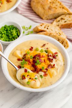 a bowl of potato soup with bacon, cheese and green onions in it next to some bread