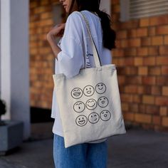 a woman carrying a tote bag with smiley faces drawn on the front and sides