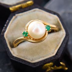 a close up of a ring with pearls and emeralds on it in a box