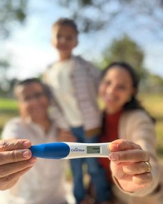 a woman holding an electronic thermometer in front of two men and a child