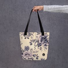 a person holding a floral bag with black handles and straps on the handle, in front of a gray background