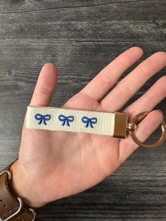 a hand holding a keychain with blue bows on it and a brown leather belt