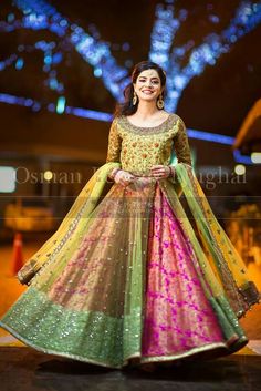 a woman in a green and pink lehenga standing on the street at night