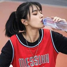 a girl drinking water from a bottle while standing on a court with her hands in her pockets