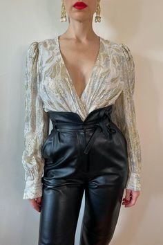 It's all couture and all mystery for the woman wearing this soft seducing silver and pearlescent wrap blouse. For maximum luxury; style with minimal makeup, a trademark red lip, and our Museum by Miss Gray couture Legacy Leather Pant. Fabric: Rayon, metallic Colour: Ivory, silver, gold Measurements: Chest 40", Waist 27", Length 21" Garment Care: Dry clean only Model: Height 5'7" - Chest 34", Waist 25", Hip 36.5" ⚜️⚜️⚜️ 10% surcharge on Etsy compared to our website due to fees 20% OFF at missgray Glamorous V-neck Blouse, Glamorous Formal V-neck Blouse, Elegant V-neck Blouse For Party Season, Elegant Gold Formal Tops, Elegant Sequined Blouse For Spring, Elegant Gold Tops For Formal Occasions, Luxury Spring Party Blouse, Spring Luxury Party Blouse, Feminine Fall Party Blouse