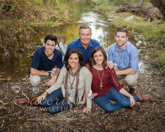 a group of people sitting next to each other in front of a river and trees