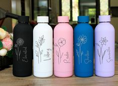 four different colored water bottles sitting on top of a wooden table