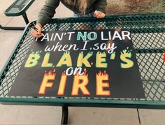 a woman sitting at a table with a sign on it that says, ain't no liar when i say blake's on fire