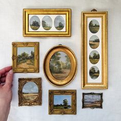 there are many paintings on the wall with gold frames around them, including trees and fields