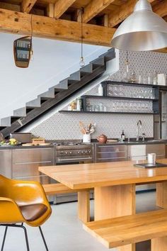 a kitchen with wooden tables and chairs next to an open staircase leading up to the second floor