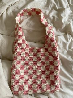 a crocheted bag laying on top of a bed covered in white and pink sheets