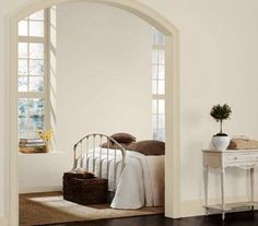 an arched doorway leads to a bedroom with a white bed and brown carpeted floor