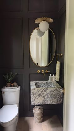 a white toilet sitting next to a bathroom sink under a round mirror on a wall