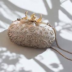 Crafted for the discerning bride, this exquisite bridal clutch is a masterpiece of elegance and artistry. Made from luxurious ivory raw silk, it showcases intricate zardozi and beadwork that creates a stunning, textured design. Each detail is meticulously hand-embroidered, reflecting the timeless tradition and skill of artisans. The clutch features a beautiful gold flower knob that serves as a statement piece, adding a touch of opulence and sophistication. The thick chain strap offers versatility, allowing you to carry it effortlessly over your shoulder or as a chic handheld piece. Inside, the clutch is lined with plush suede, ensuring your essentials are kept safe and adding a touch of softness to the overall design. This dreamy clutch is not just an accessory but a cherished keepsake for Zardozi Work, Bridal Clutch, Ivory Bridal, Textured Design, Vintage Bridal, Gold Flower, Texture Design, Gold Flowers, Raw Silk