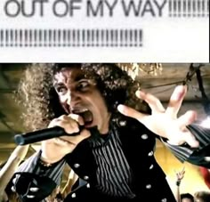 a man with curly hair singing into a microphone and holding his hands up in the air