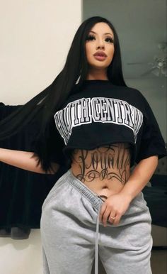 a woman with long black hair wearing grey sweatpants and a crop top that says,