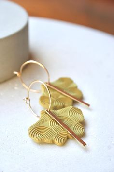 two pairs of earrings sitting on top of a white table next to a cup and paper