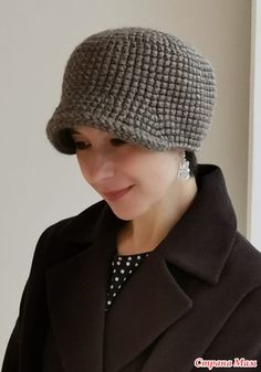 a woman wearing a gray crochet hat and coat looking at her cell phone