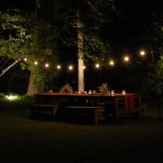 an outdoor dining area lit up at night with string lights strung from the trees and on the ground