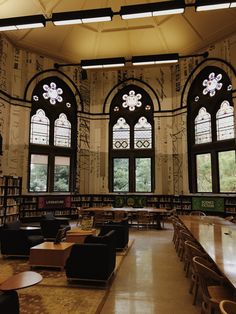 an empty library with tables and chairs in front of two large windows that have stained glass on them