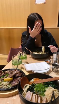 a woman sitting at a table covered in food with chopsticks covering her face