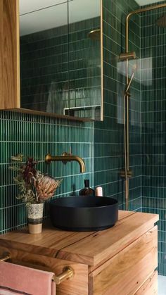 a bathroom with green tiled walls and wooden cabinet, black bowl sink and gold faucet