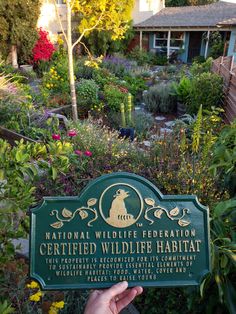 a person holding up a sign that says national wildlife foundation certified wildlife habitat in front of a garden