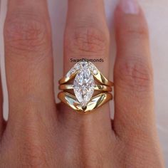 a woman's hand wearing a gold ring with a pear shaped diamond in the center